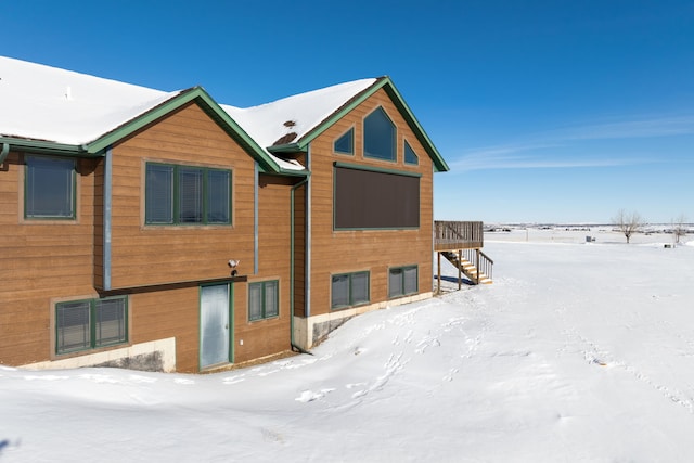 snow covered house with stairway and a wooden deck