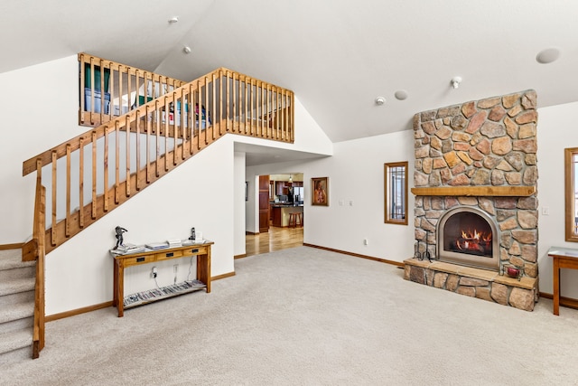 living area featuring baseboards, stairs, a stone fireplace, carpet floors, and high vaulted ceiling