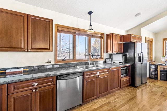 kitchen with stainless steel appliances, a sink, light wood-type flooring, brown cabinetry, and decorative light fixtures