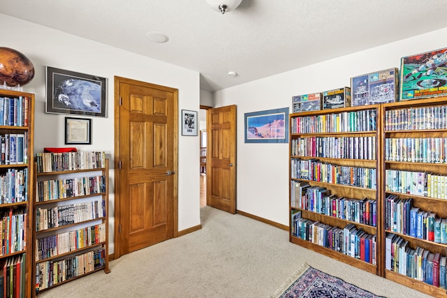 living area featuring light carpet, wall of books, and baseboards