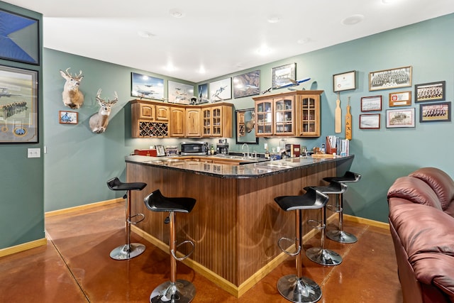 bar with baseboards, stainless steel microwave, indoor wet bar, finished concrete floors, and a sink