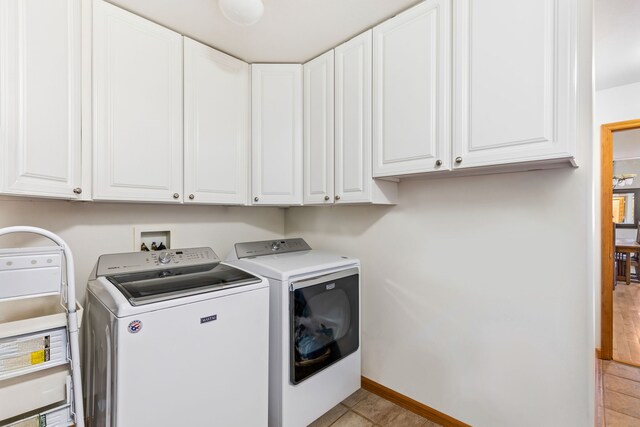 clothes washing area with light tile patterned floors, independent washer and dryer, cabinet space, and baseboards