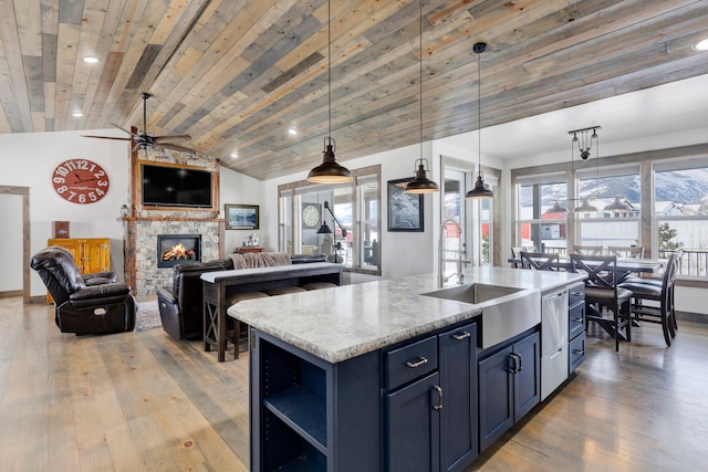 kitchen with decorative light fixtures, open floor plan, a kitchen island with sink, light stone countertops, and blue cabinets