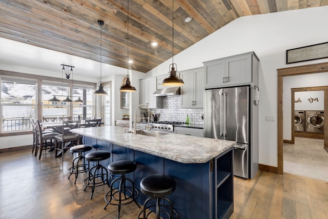 kitchen featuring decorative light fixtures, stainless steel appliances, a kitchen island with sink, a sink, and washer and dryer