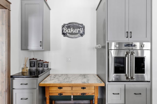 kitchen featuring light stone countertops, gray cabinetry, and oven