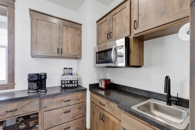 kitchen featuring stainless steel microwave, dark countertops, and a sink