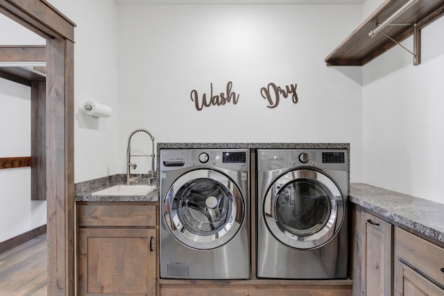 laundry room with light wood-style floors, cabinet space, a sink, and washer and clothes dryer