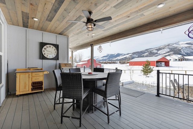 snow covered deck with a ceiling fan, outdoor dining area, and a mountain view