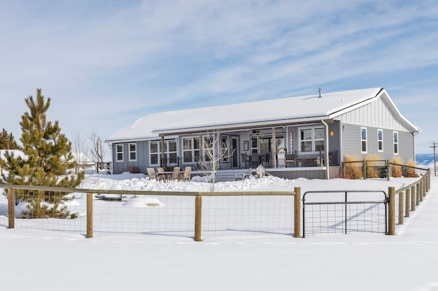 snow covered back of property with a fenced front yard, covered porch, and board and batten siding