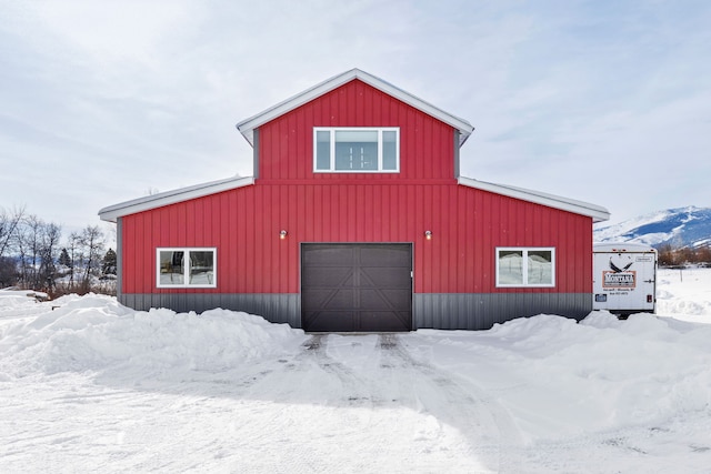 snow covered structure featuring a barn, a mountain view, and an outbuilding