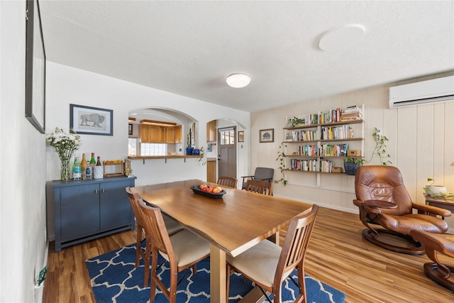 dining space with arched walkways, an AC wall unit, a textured ceiling, and wood finished floors