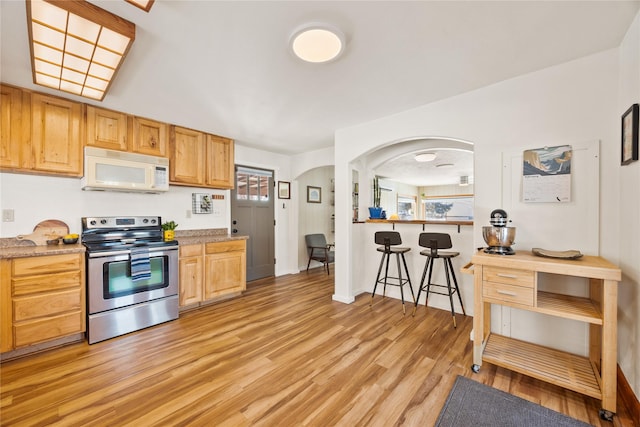 kitchen with white microwave, light wood-style floors, light countertops, a kitchen bar, and stainless steel range with electric stovetop