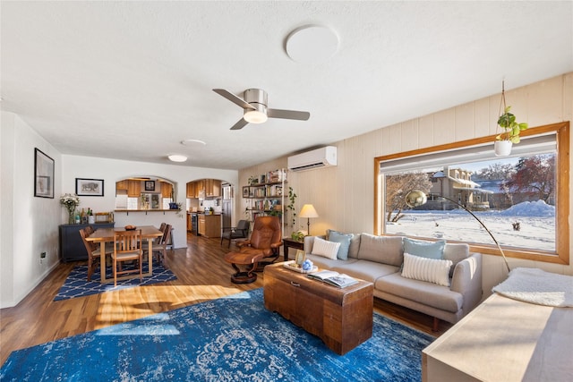 living room featuring a ceiling fan, arched walkways, dark wood-style flooring, and a wall mounted air conditioner