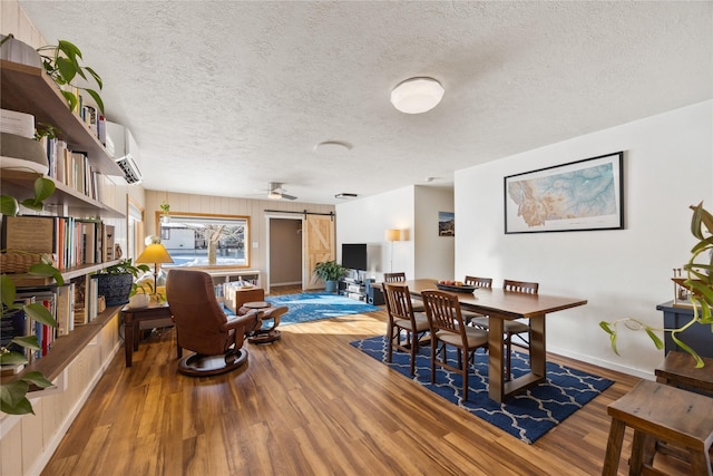 dining room with wood finished floors, a textured ceiling, baseboards, and a barn door