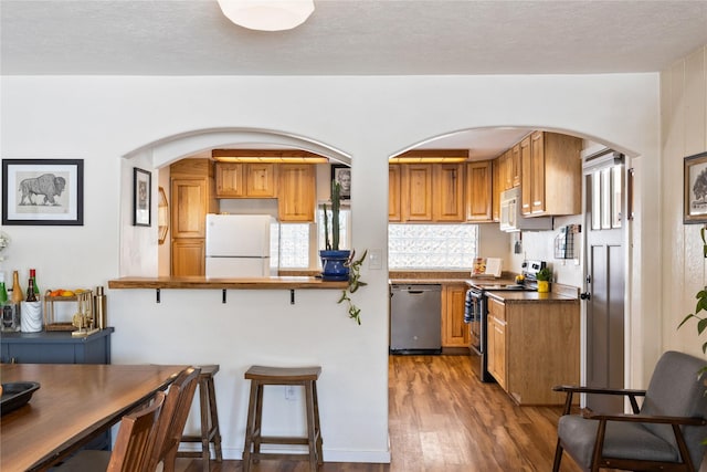 kitchen featuring a breakfast bar, stainless steel appliances, dark countertops, brown cabinetry, and dark wood-type flooring