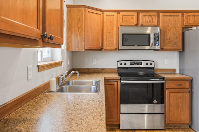 kitchen featuring appliances with stainless steel finishes, brown cabinetry, and a sink