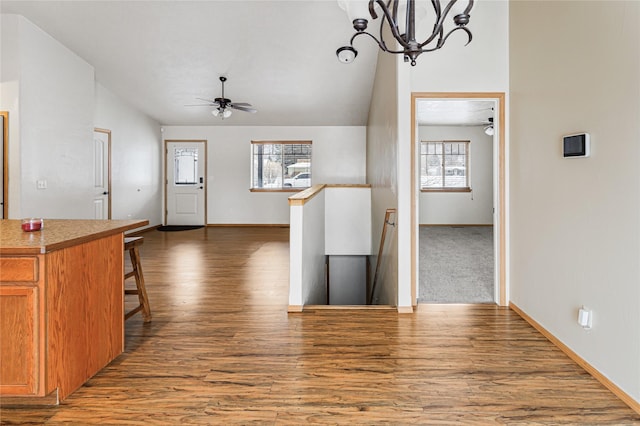 kitchen with brown cabinetry, dark wood-style floors, a breakfast bar area, vaulted ceiling, and pendant lighting