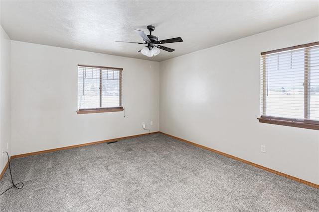 empty room featuring a textured ceiling, ceiling fan, carpet floors, visible vents, and baseboards