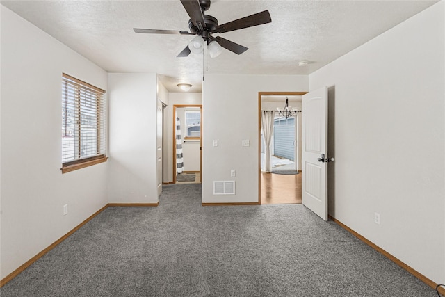 unfurnished bedroom featuring a textured ceiling, ceiling fan with notable chandelier, carpet flooring, visible vents, and baseboards