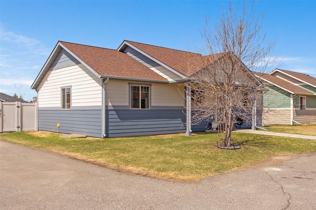 view of front of home featuring roof with shingles, fence, and a front lawn