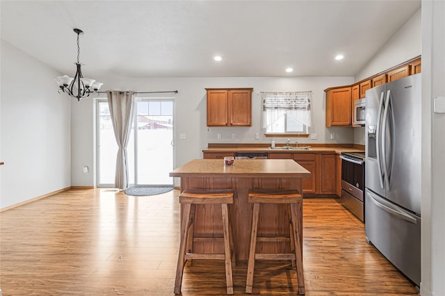 kitchen with a kitchen island, a breakfast bar area, stainless steel appliances, light wood-type flooring, and a sink