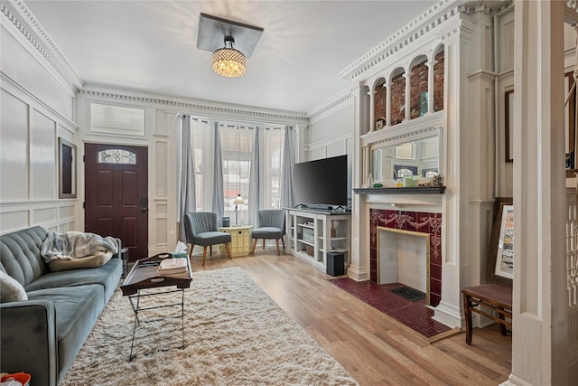 living room with light wood-style flooring, ornamental molding, a decorative wall, and a tiled fireplace