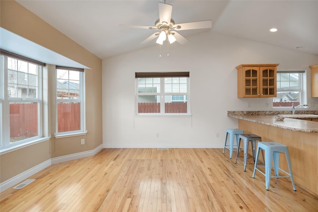 kitchen with lofted ceiling, light wood-style flooring, glass insert cabinets, a kitchen breakfast bar, and a sink