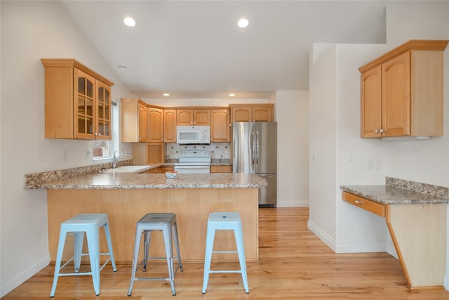 kitchen with a peninsula, white appliances, a sink, a kitchen bar, and glass insert cabinets