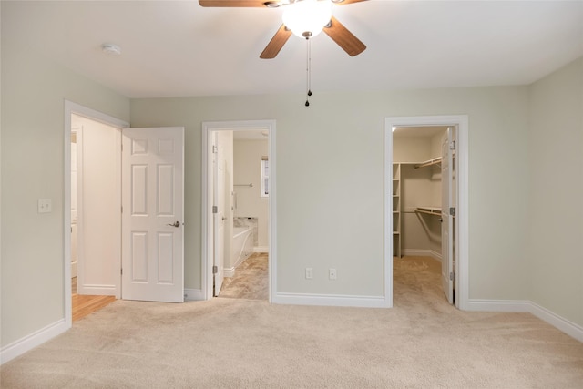 unfurnished bedroom featuring a closet, light colored carpet, a spacious closet, ensuite bathroom, and baseboards