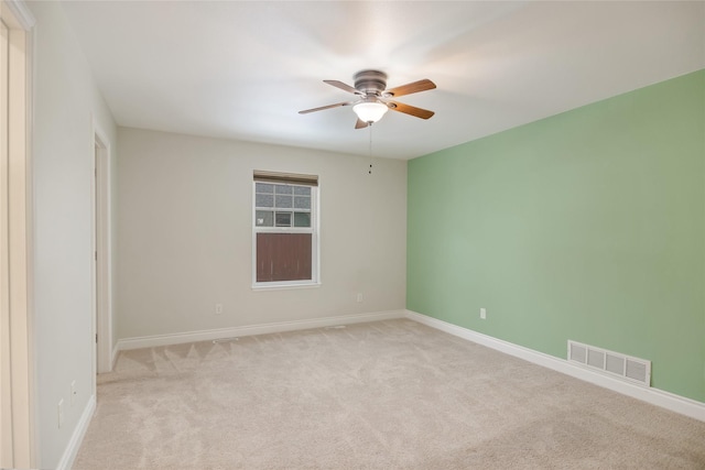 spare room featuring light carpet, ceiling fan, visible vents, and baseboards