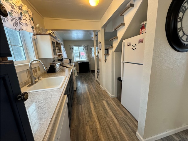 kitchen with white appliances, decorative columns, dark wood-style floors, and a sink