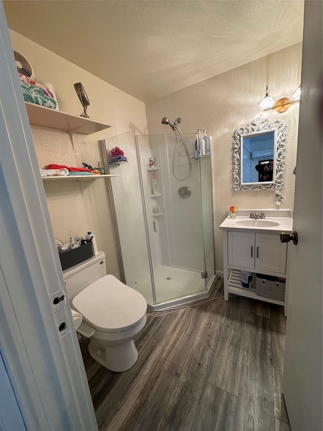 bathroom with toilet, a shower stall, a textured ceiling, and wood finished floors