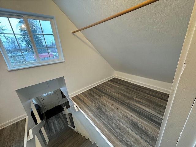 stairway with lofted ceiling, a textured ceiling, wood finished floors, and baseboards