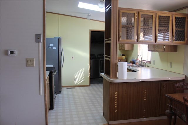 kitchen with a peninsula, separate washer and dryer, a sink, light floors, and glass insert cabinets