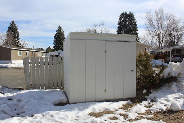 snow covered structure with an outdoor structure, fence, and a storage unit