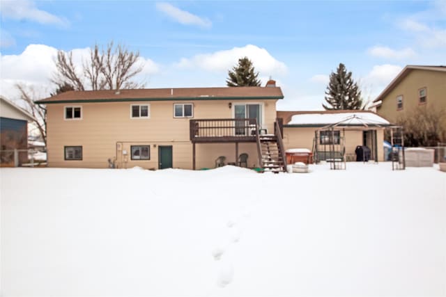 snow covered house with a chimney, a deck, and stairs