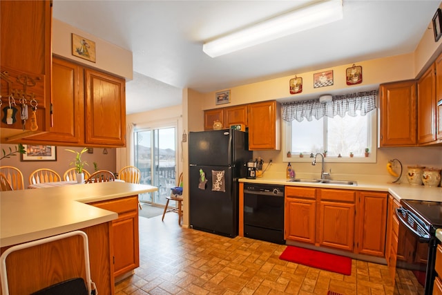 kitchen with brick floor, a sink, light countertops, brown cabinets, and black appliances