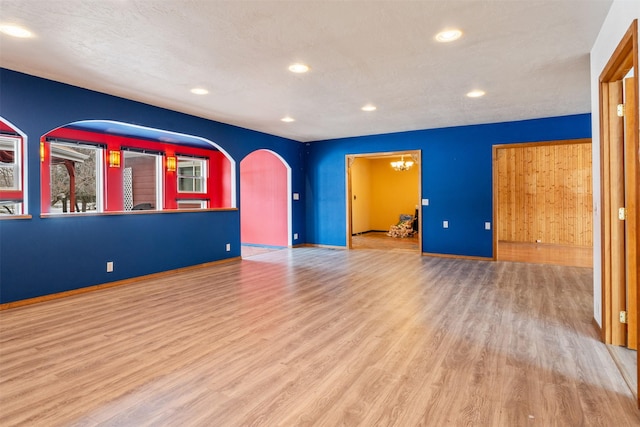 empty room featuring light wood-style floors, arched walkways, baseboards, and recessed lighting