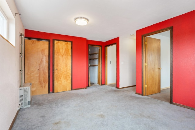 unfurnished bedroom with multiple closets, heating unit, light colored carpet, and baseboards