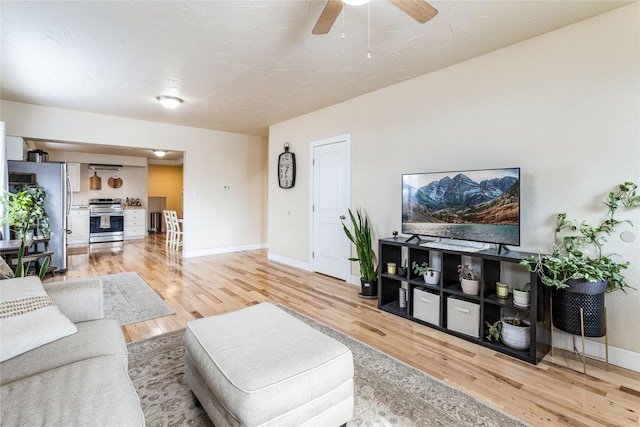 living area with ceiling fan, light wood-style flooring, and baseboards