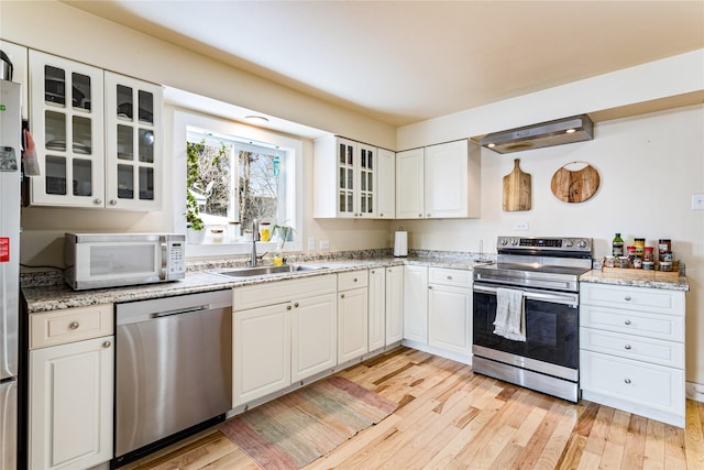 kitchen featuring a sink, white cabinetry, light wood-style floors, appliances with stainless steel finishes, and glass insert cabinets