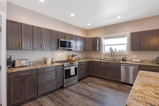 kitchen with light stone counters, recessed lighting, dark wood-type flooring, a sink, and appliances with stainless steel finishes