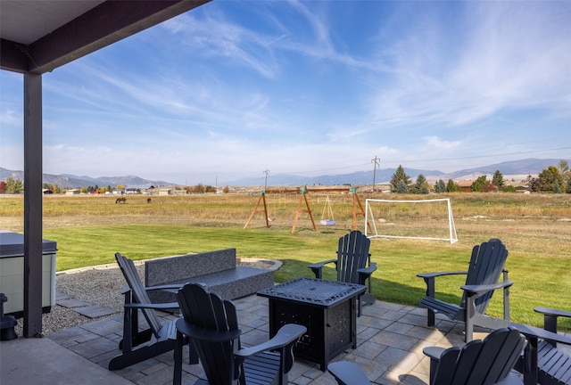 view of patio featuring an outdoor fire pit, a mountain view, a playground, and a rural view