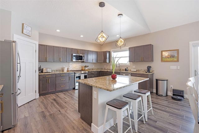 kitchen featuring light stone counters, a breakfast bar, stainless steel appliances, light wood-style floors, and a kitchen island