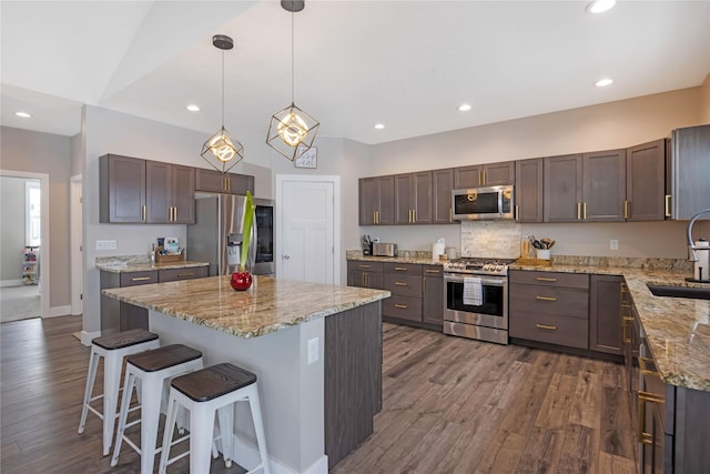 kitchen with a breakfast bar, dark wood-style flooring, appliances with stainless steel finishes, a sink, and a kitchen island