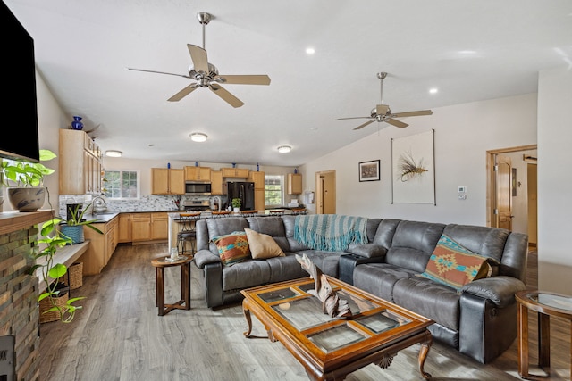 living room with a ceiling fan, light wood-type flooring, and vaulted ceiling