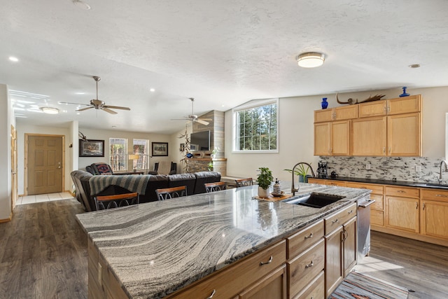 kitchen featuring a kitchen island with sink, a sink, vaulted ceiling, backsplash, and dark wood finished floors