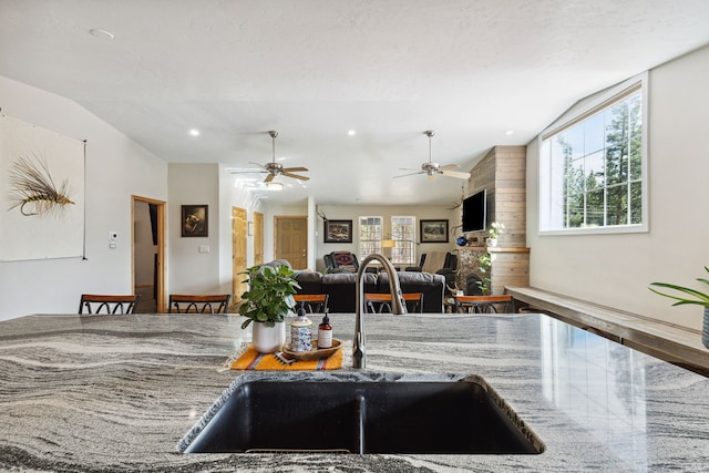 kitchen featuring lofted ceiling, stone countertops, a ceiling fan, a sink, and a textured ceiling