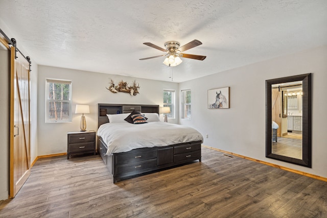 bedroom with a barn door, multiple windows, baseboards, and wood finished floors