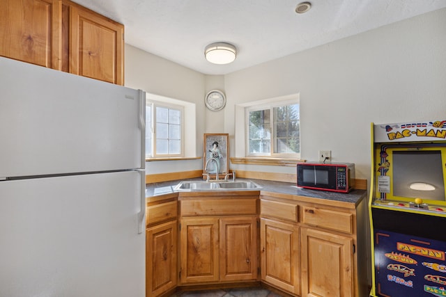 kitchen with freestanding refrigerator, brown cabinets, and a sink